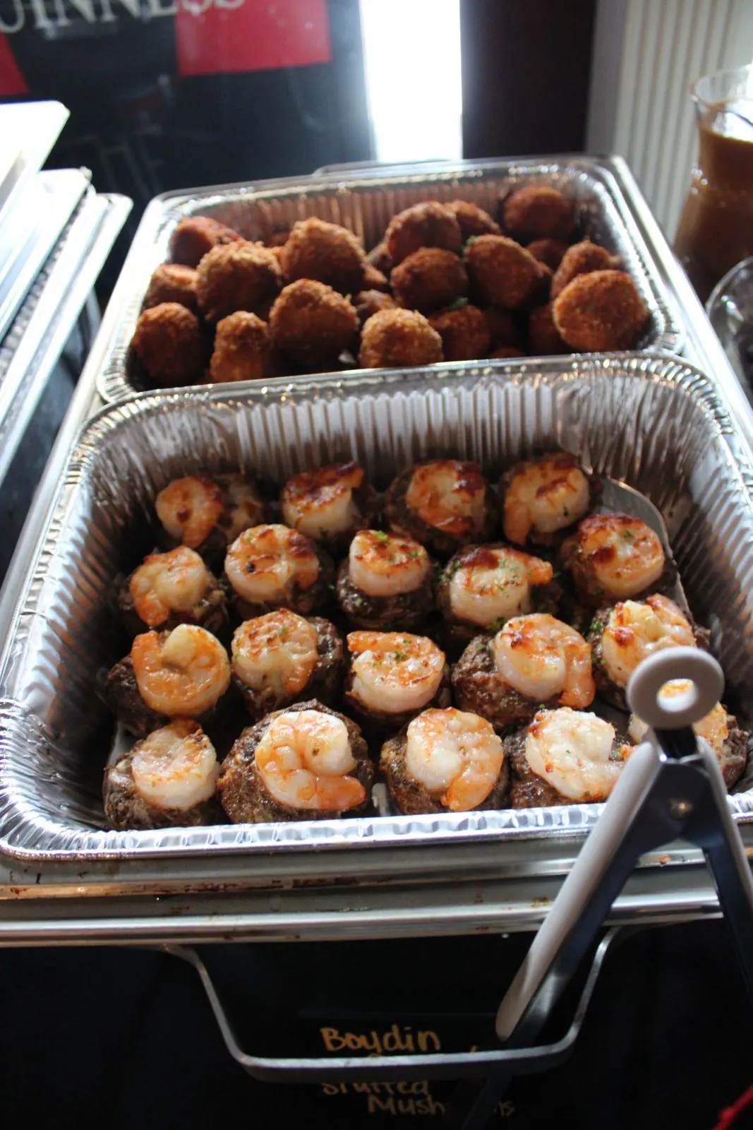 Boudin-stuffed mushrooms topped with shrimp next to a pan of boudin balls