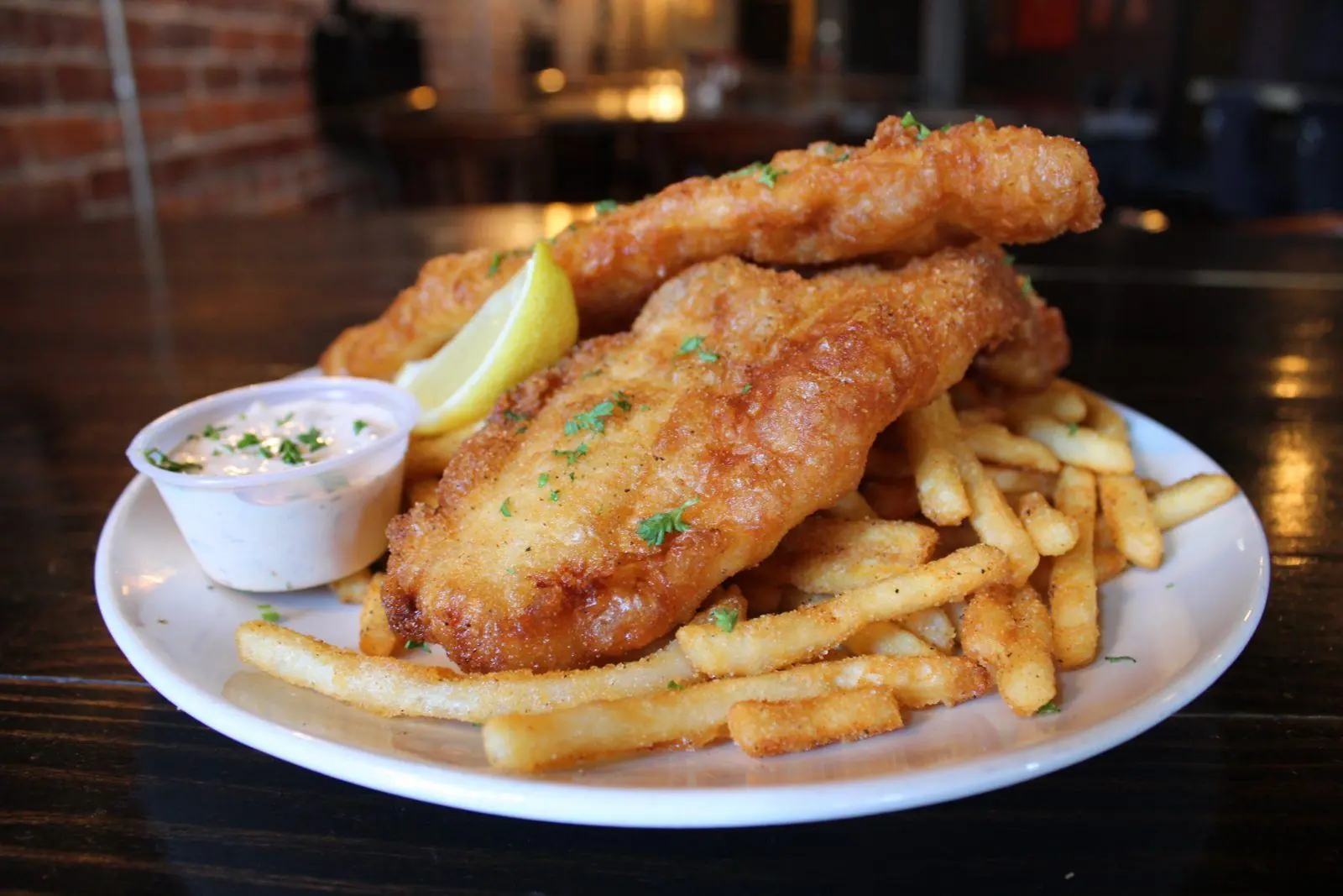 Two golden fried fish fillets over seasoned fries with tartar sauce and lemon